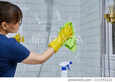 Woman cleaning bathroom, washing glass in shower Woman cleaning bathroom, washing glass in shower 111355221