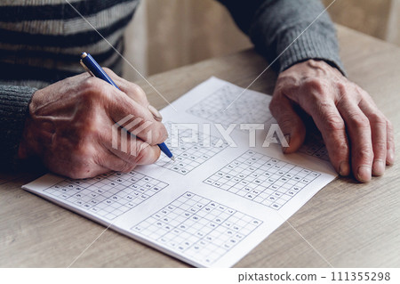 Senior solves sudoku or a crossword puzzle to slow the progressi Senior solves sudoku or a crossword puzzle to slow the progressi 111355298