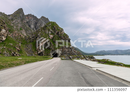 Road curves into rock tunnel with tranquil Nordic sea overlook by Bleiksveien, inviting journey Road curves into rock tunnel with tranquil Nordic sea overlook by Bleiksveien, inviting journey 111356097