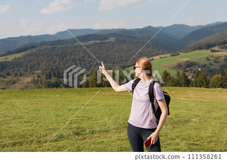 Blonde 30s girl in sunglasses pointing finger on mountains background. Young female with backpack hiking in nature. Beautiful woman walking in sport clothes. Freedom and active lifestyle concept Blonde 30s girl in sunglasses pointing finger on mountains background. Young female with backpack hiking in nature. Beautiful woman walking in sport clothes. Freedom and active lifestyle concept 111358261