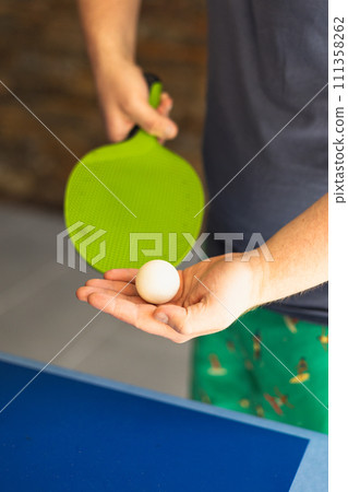 A man is playing ping pong. He holds a white ball and a green racket in his hands. Table tennis. The concept of sport and healthy lifestyle. 111358262