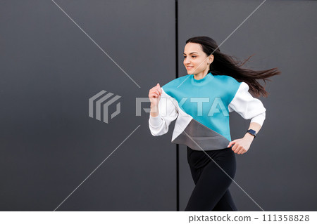 Young woman with fit body jumping and running against dark wall background. Female model in sportswear exercising outdoors. 111358828