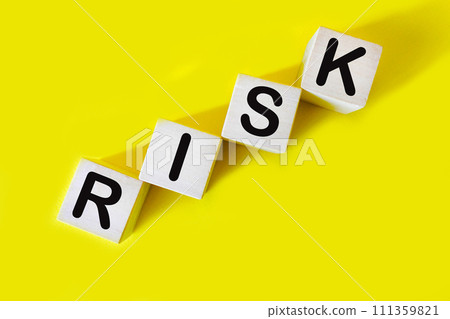 The word RISK. Wooden letter cubes isolated on a yellow background with copy space available.  111359821