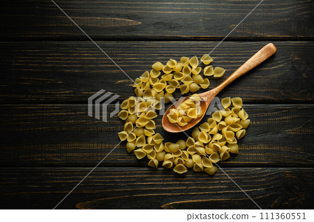 Shell-type pasta on an antique dark table and in a spoon before preparing breakfast. Space for a recipe or menu for a restaurant Shell-type pasta on an antique dark table and in a spoon before preparing breakfast. Space for a recipe or menu for a restaurant 111360551