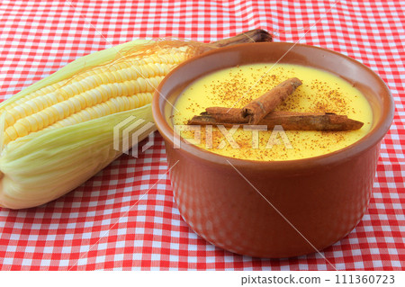 curau, cream of sweet corn and dessert typical of the Brazilian cuisine, with cinnamon placed in a ceramic bowl on a checkered tablecloth. 111360723