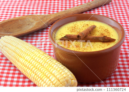 curau, cream of sweet corn and dessert typical of the Brazilian cuisine, with cinnamon placed in a ceramic bowl on a checkered tablecloth. 111360724