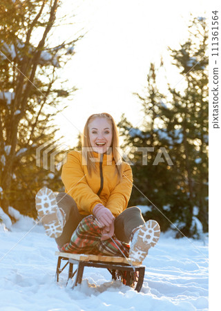 Happy young woman riding a sledge in winter forest at sunset. Happy young woman riding a sledge in winter forest at sunset. 111361564