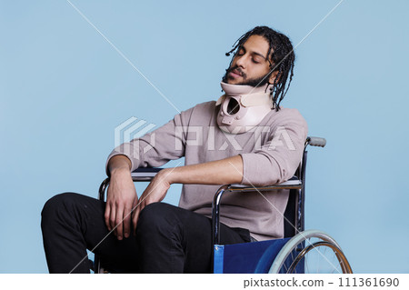 Arab man wearing cervical collar and sleeping while sitting in wheelchair. Young exhausted patient with closed eyes recovering from accident, using neck brace for spinal protection Arab man wearing cervical collar and sleeping while sitting in wheelchair. Young exhausted patient with closed eyes recovering from accident, using neck brace for spinal protection 111361690