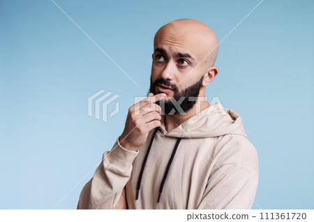 Arab man making decision, touching chin thoughtfully and looking away. Young bald bearded person with pensive facial expression contemplating, thinking about problem solving Arab man making decision, touching chin thoughtfully and looking away. Young bald bearded person with pensive facial expression contemplating, thinking about problem solving 111361720