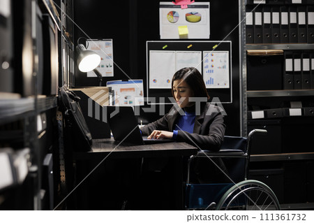 Professional businesswoman accountancy employee in wheelchair writing budget plan and accountancy strategy on laptop. Asian woman in repository filled with document folders and flowcharts Professional businesswoman accountancy employee in wheelchair writing budget plan and accountancy strategy on laptop. Asian woman in repository filled with document folders and flowcharts 111361732