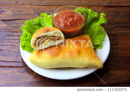 meat esfiha (sfiha) of Arab origin traditionally adapted for the Brazilian cuisine on plate on rustic wooden table meat esfiha (sfiha) of Arab origin traditionally adapted for the Brazilian cuisine on plate on rustic wooden table 111362073