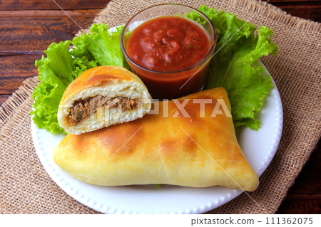 meat esfiha (sfiha) of Arab origin traditionally adapted for the Brazilian cuisine on plate on rustic wooden table meat esfiha (sfiha) of Arab origin traditionally adapted for the Brazilian cuisine on plate on rustic wooden table 111362075
