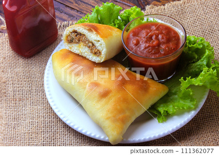 meat esfiha (sfiha) of Arab origin traditionally adapted for the Brazilian cuisine on plate on rustic wooden table meat esfiha (sfiha) of Arab origin traditionally adapted for the Brazilian cuisine on plate on rustic wooden table 111362077