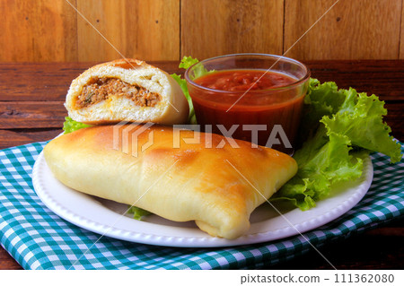 meat esfiha (sfiha) of Arab origin traditionally adapted for the Brazilian cuisine on plate on rustic wooden table meat esfiha (sfiha) of Arab origin traditionally adapted for the Brazilian cuisine on plate on rustic wooden table 111362080