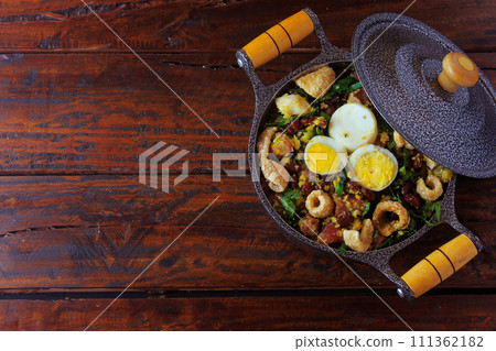 Feijao Tropeiro typical dish of Brazilian cuisine, made with beans, bacon, sausage, collard greens, eggs, on rustic wooden table. Feijao Tropeiro typical dish of Brazilian cuisine, made with beans, bacon, sausage, collard greens, eggs, on rustic wooden table. 111362182