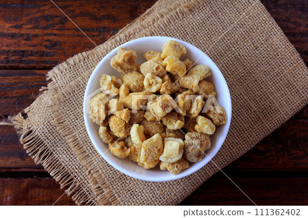 pork rinds fried in ceramic bowl on rustic wooden table in restaurant 111362402