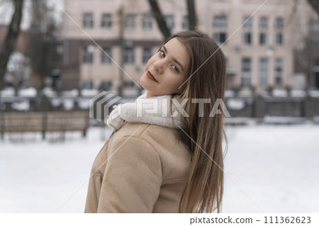 Portrait of long-haired brunette girl in beige sheepskin coat in winter outdoors. Young woman with light makeup on walk 111362623