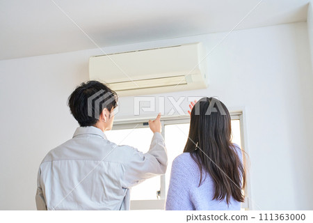 一個穿著工作服的男人站在空調前,一個女人在看著它 一個穿著工作服的男人站在空調前,一個女人在看著它 111363000