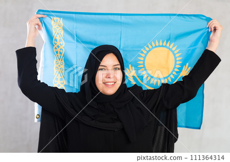 Happy young woman dressed in traditional islamic clothes with kazakh flag Happy young woman dressed in traditional islamic clothes with kazakh flag 111364314