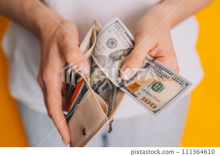 Lady putting dollar bills into a white wallet against a yellow background Lady putting dollar bills into a white wallet against a yellow background 111364610
