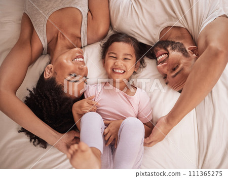 Above, family and child happy on bed smile, laugh and bonding on weekend. Mom, dad and parents with kid in pajamas enjoying quality time, being playful and fun together in bedroom in the morning. 111365275