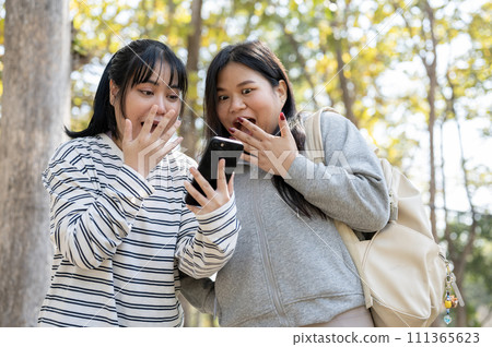Two amazed young Asian female college students are surprised by unbelievable news on a smartphone. Two amazed young Asian female college students are surprised by unbelievable news on a smartphone. 111365623