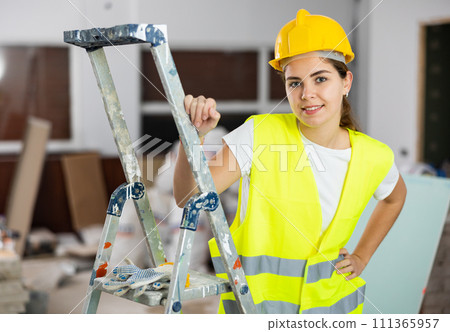 Enthusiastic female builder in yellow workwear inside house under construction Enthusiastic female builder in yellow workwear inside house under construction 111365957