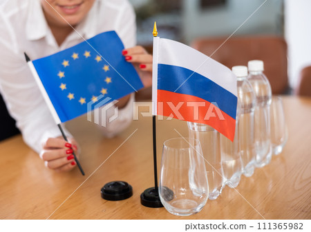 Unrecognizable girl sets midget flags of Russia and European Union before international negotiations Unrecognizable girl sets midget flags of Russia and European Union before international negotiations 111365982