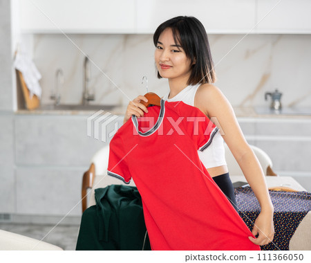 Happy young Asian girl trying to choose a dress in the kitchen Happy young Asian girl trying to choose a dress in the kitchen 111366050