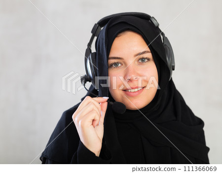 Happy young woman dressed in traditional islamic clothes with headphones with microphone on 111366069