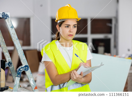 Focused female safety inspector making notes at construction site Focused female safety inspector making notes at construction site 111366151