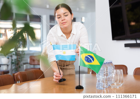 Young female assistant putting up brazilian and argentinian flags on table for international negotiations Young female assistant putting up brazilian and argentinian flags on table for international negotiations 111366171
