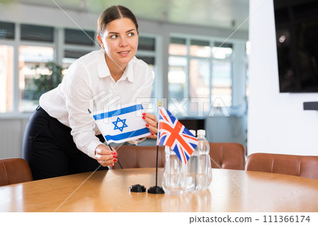 Positive young woman putting little flag of Israel on table next to the flag of Great Britain 111366174