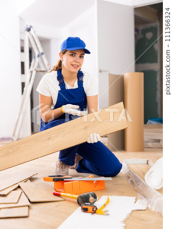 Repair in the room - woman puts laminate on the floor and checks horizontal level Repair in the room - woman puts laminate on the floor and checks horizontal level 111366324