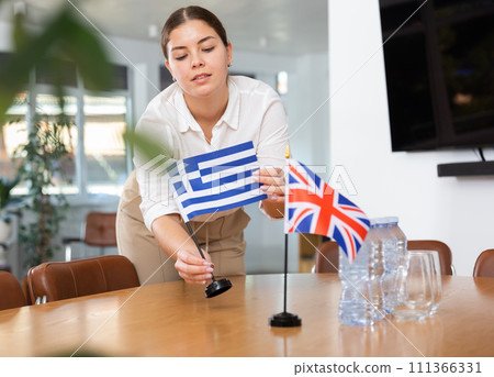 Preparing for business presentation - secretary places flags of Greece and Great Britain on negotiating table 111366331