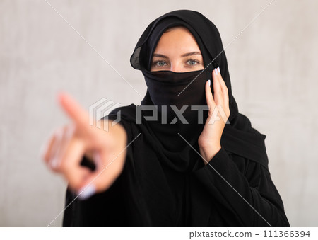 woman with her face covered by burka points her hand to side woman with her face covered by burka points her hand to side 111366394