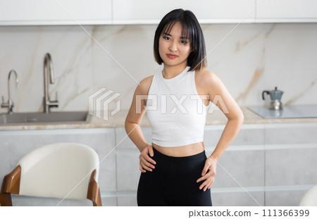 Smiling young Asian girl standing at table in the kitchen Smiling young Asian girl standing at table in the kitchen 111366399