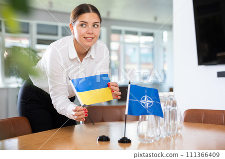 Businesswoman arranging the flags of NATO (OTAN) and Ukrain for presentation and negotiations 111366409