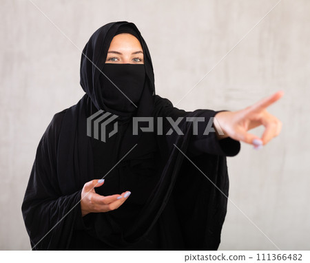 woman with her face covered by burka points her hand to side woman with her face covered by burka points her hand to side 111366482