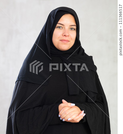 young joyful Muslim woman in traditional hijab clothes poses on gray background. 111366517