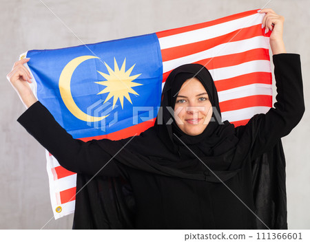 Happy young woman dressed in traditional islamic clothes with malaysian flag 111366601