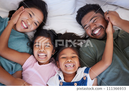 Happy, smile and portrait of family from above in bed bonding together in a bedroom at home. Happiness, love and interracial parents lying with girl children in holiday house room while on vacation. 111366933