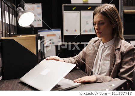 Police officer preparing to leave job after working overtime at missing person case in evidence room. Private detective analyzing crime scene report, searching for new clues. Criminology report Police officer preparing to leave job after working overtime at missing person case in evidence room. Private detective analyzing crime scene report, searching for new clues. Criminology report 111367717