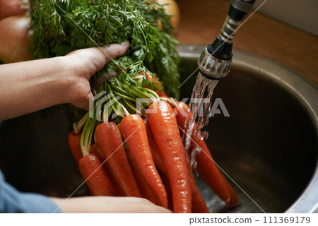 Carrot, water and cleaning vegetables with hands in kitchen, hygiene and health with chef cooking food. Nutrition, person with vegan or vegetarian meal, wash produce at sink for catering and dinner 111369179