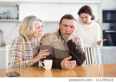 Family members quarreling in the kitchen and old woman trying to calm angry man Family members quarreling in the kitchen and old woman trying to calm angry man 111369228