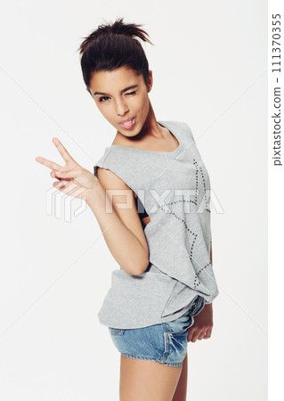 Portrait, woman and peace sign with tongue in studio for fun, playful and humour with confidence. Female person, emoji and face with gesture for pose, fashion or expression on white background 111370355