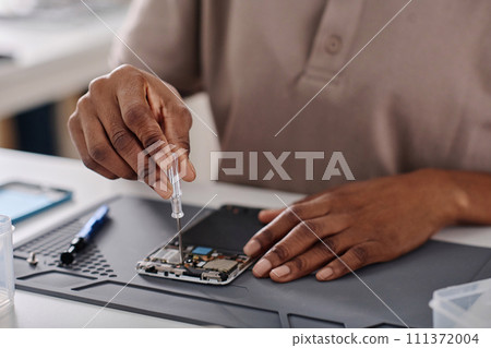 Hands of unrecognizable black specialist tightening cogs in disassembled phone with little screwdriver Hands of unrecognizable black specialist tightening cogs in disassembled phone with little screwdriver 111372004