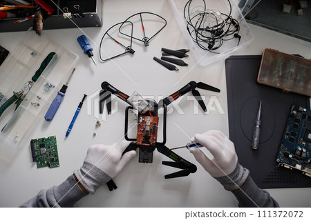 Flat lay shot of hands of unrecognizable repairman fixing broken quadcopter with screwdriver Flat lay shot of hands of unrecognizable repairman fixing broken quadcopter with screwdriver 111372072