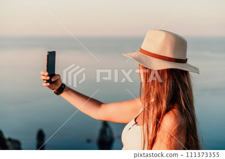 Selfie woman in hat, white tank top and shorts makes selfie shot mobile phone post photo social network outdoors on sea background beach people vacation lifestyle travel concept. Selfie woman in hat, white tank top and shorts makes selfie shot mobile phone post photo social network outdoors on sea background beach people vacation lifestyle travel concept. 111373355