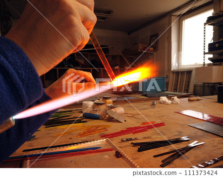Close up of artist hands creating glass pendant with lampworking technique 111373424
